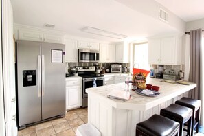 A modern kitchen with white cabinetry, stainless steel appliances, a central island with stools, and a bag of chips on the counter. - Glorious Cabin with Fantastic Lake Sights in Hot Springs, Arkansas (Hot Springs)