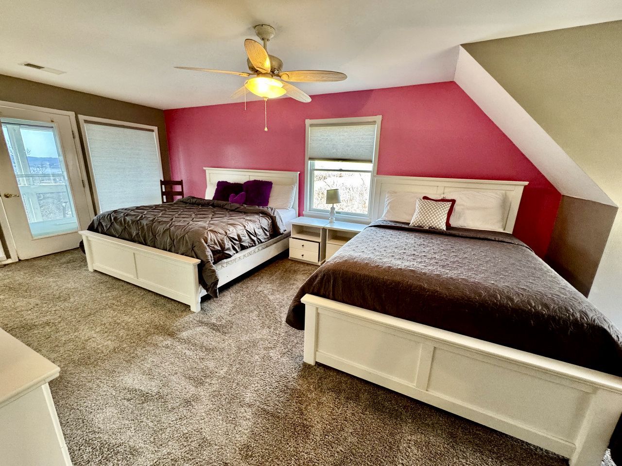 A bedroom with two beds, a ceiling fan, and a view of the outside.