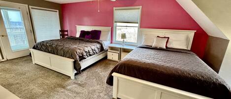 A bedroom with two beds, a ceiling fan, and a view of the outside.