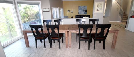 A dining area with a wooden table and chairs, a staircase, and a view of the outdoors.