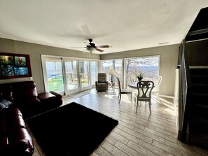 A spacious living room with a ceiling fan, a fireplace, and a view through large sliding glass doors.