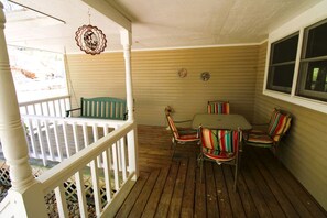 Eine überdachte Veranda mit Holzdeck, weißer Brüstung, Tisch und Stühlen sowie einem Fenster.