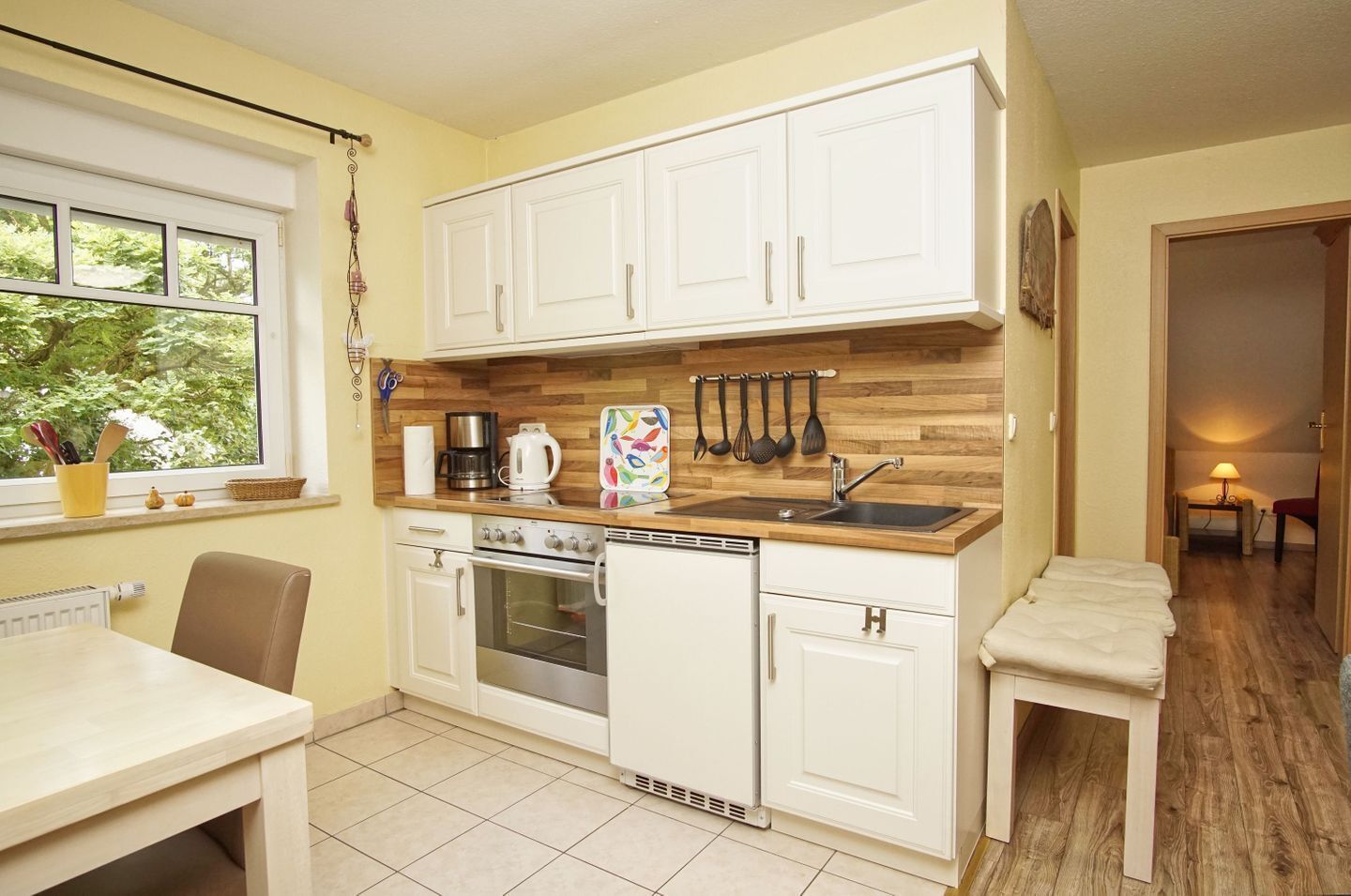 A compact kitchen with white cabinets, a stove, a sink, and a window with a view of greenery.