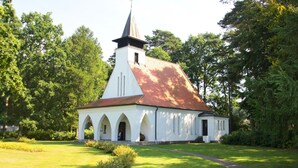 A church with a steeple, arched windows, and a red roof, surrounded by greenery. - Quietly situated vacation apartment - Ferienhaus Weingarten FeWo zum Fischer - (Baabe)