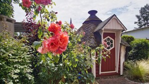 A garden with blooming roses and a small red building with a conical roof. - Quietly situated vacation apartment - Ferienhaus Weingarten FeWo zum Fischer - (Baabe)