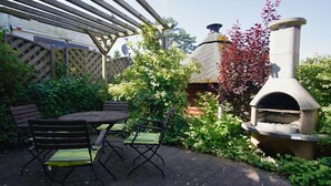 Eine Terrasse mit rundem Tisch und Stühlen, einem Steinofen und einer Holzpergola.
