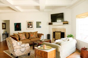 A living room with a sofa, armchair, fireplace, television, and artwork on the wall. - Outstanding Cottage with Swimming Pool in Hot Springs, Arkansas (Hot Springs)