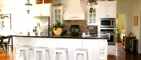 A kitchen with white cabinetry, a central island with bar stools, and various appliances.