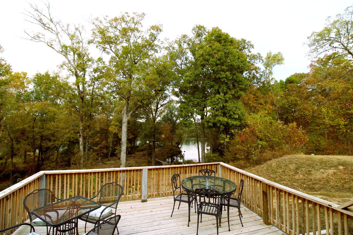 A wooden deck with outdoor furniture, surrounded by trees and a lake.