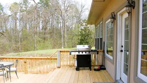 Eine Terrasse mit Grill, Sitzgelegenheit und Blick auf den umliegenden Wald.