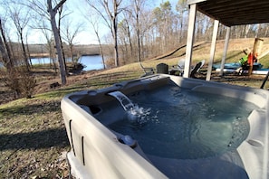 A hot tub with a waterfall feature, surrounded by a grassy area and trees, with a lake and chairs in the background. - Outstanding Cottage with Swimming Pool in Hot Springs, Arkansas (Hot Springs)
