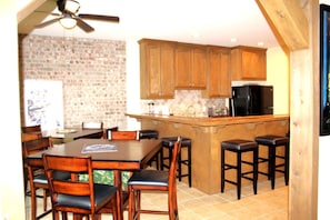 A kitchen with wooden cabinets, a black refrigerator, and a bar area with stools. - Outstanding Cottage with Swimming Pool in Hot Springs, Arkansas (Hot Springs)