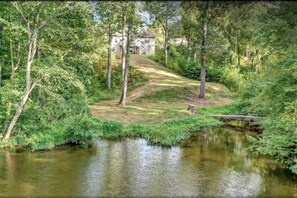 A serene riverside setting with a bridge, lush greenery, and a building in the background. - Outstanding Cottage with Swimming Pool in Hot Springs, Arkansas (Hot Springs)