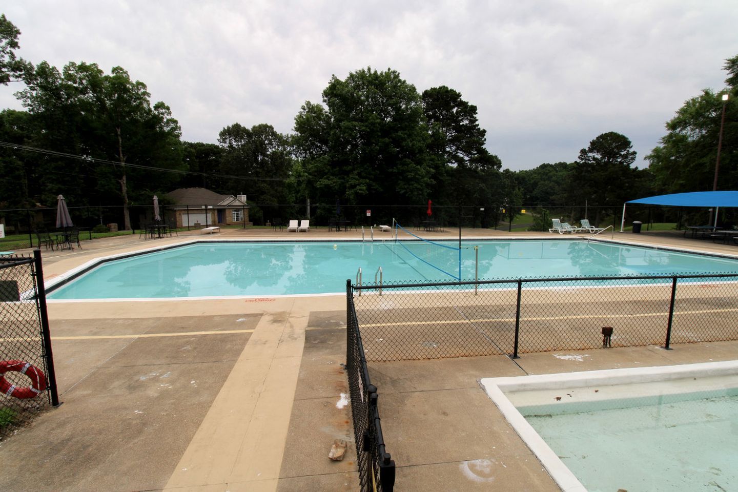 A rectangular swimming pool with a surrounding fence, lounge chairs, and umbrellas.