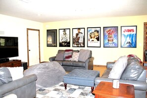 Ein Wohnzimmer mit Fernseher, Ledersofas, einem Couchtisch und Filmplakaten an der Wand.