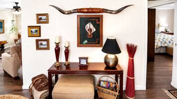 A living room with a wooden table, a lamp, a large horn decoration, framed pictures, and a wicker basket.
