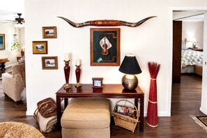 A living room with a wooden table, a lamp, a large horn decoration, framed pictures, and a wicker basket.