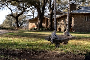 A rustic wooden swing set in a grassy yard with a stone building in the background. - Lovely Cottage Rental with Waterfall on San Gabriel River near Austin, Texas (Georgetown)