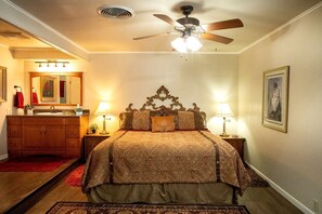 A bedroom with a bed, two bedside tables with lamps, a ceiling fan, a mirror, a red rug, and a framed picture on the wall.