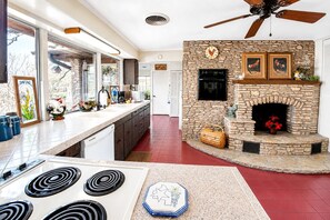 A kitchen with a stone fireplace, a ceiling fan, and a large window.