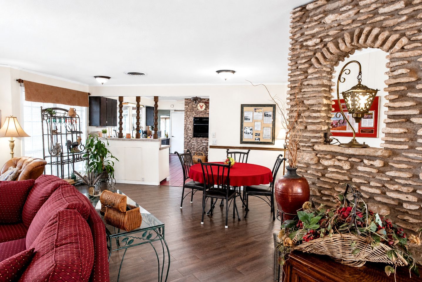 A living room with a red sofa, a dining area with a red table, and a kitchen area with a stone wall.
