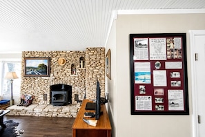 A stone fireplace with a modern TV, a framed picture above it, and a bulletin board with various notices. - Romantic Luxury Cottage Rental for Two with Fireplace in Texas Hill Country (Georgetown)
