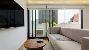 Een moderne woonkamer met een bank, een ronde houten salontafel en een aan de muur bevestigde televisie.
