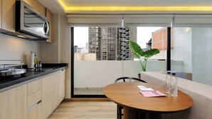 Une cuisine moderne dotée d’un four à micro-ondes encastré, un coin repas avec une table ronde et une grande fenêtre offrant une vue sur le paysage urbain.
