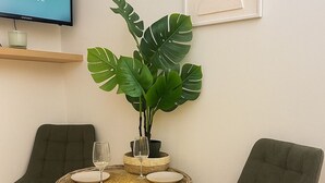 Ein Essbereich mit einem runden Tisch, zwei Stühlen, einer Zimmerpflanze, einer Kerze und einem Fernseher auf einem Regal.