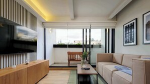 Una sala de estar moderna con televisor de pantalla plana, consola de madera, sofá color crema y vistas amplias a través de ventanas grandes.