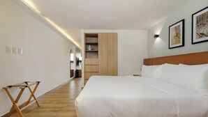 Habitación de hotel con una cama grande, suelo de madera, armario empotrado y una pequeña mesa.