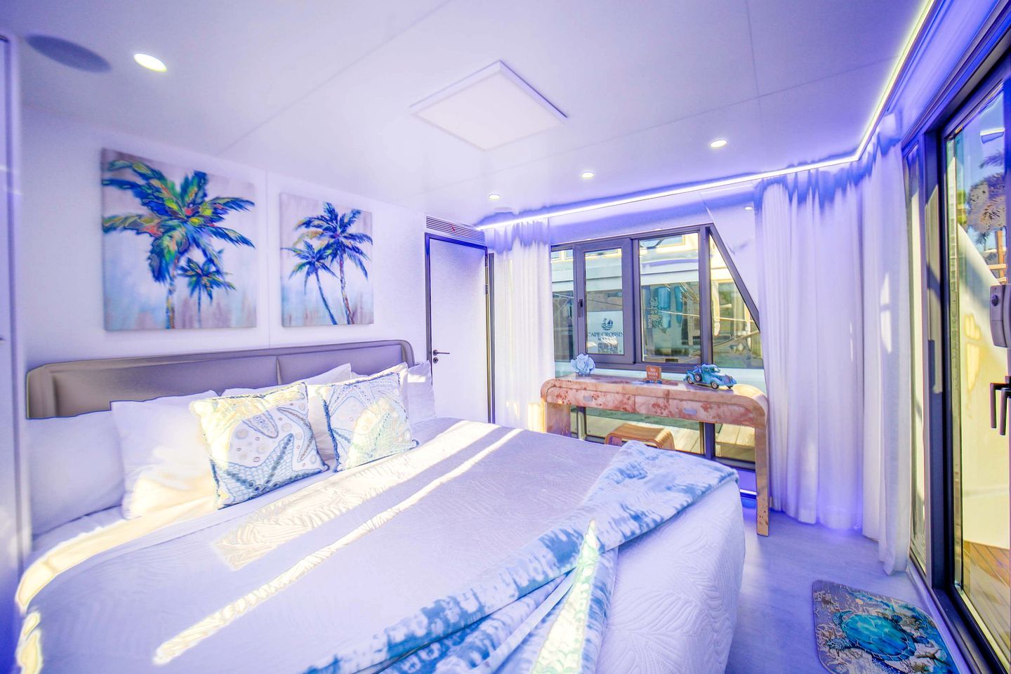 A modern bedroom with a large bed, a small table with decorative items, and a view of the outside through a glass door.