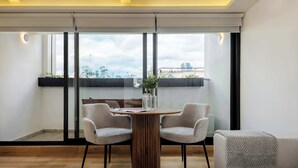 Een moderne eethoek met een ronde houten tafel, twee grijs gestoffeerde stoelen en een vaas met bloemen.
