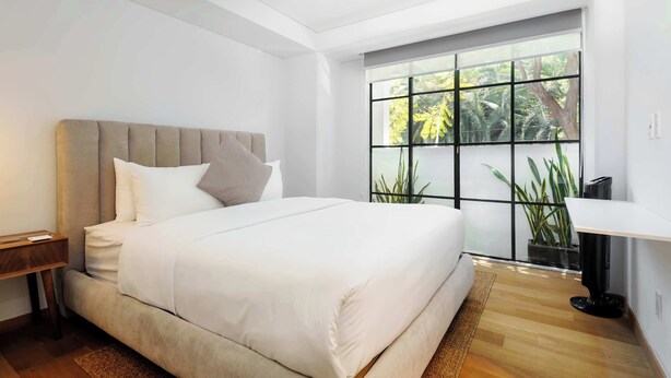 Un dormitorio moderno con una cama grande, una mesita de noche, un escritorio y una ventana con vista a zonas verdes.