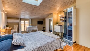 Een slaapkamer met dakraam, een bed met beddengoed met dessin, een bureau met stoel, een televisie en een douchecabine van glas.