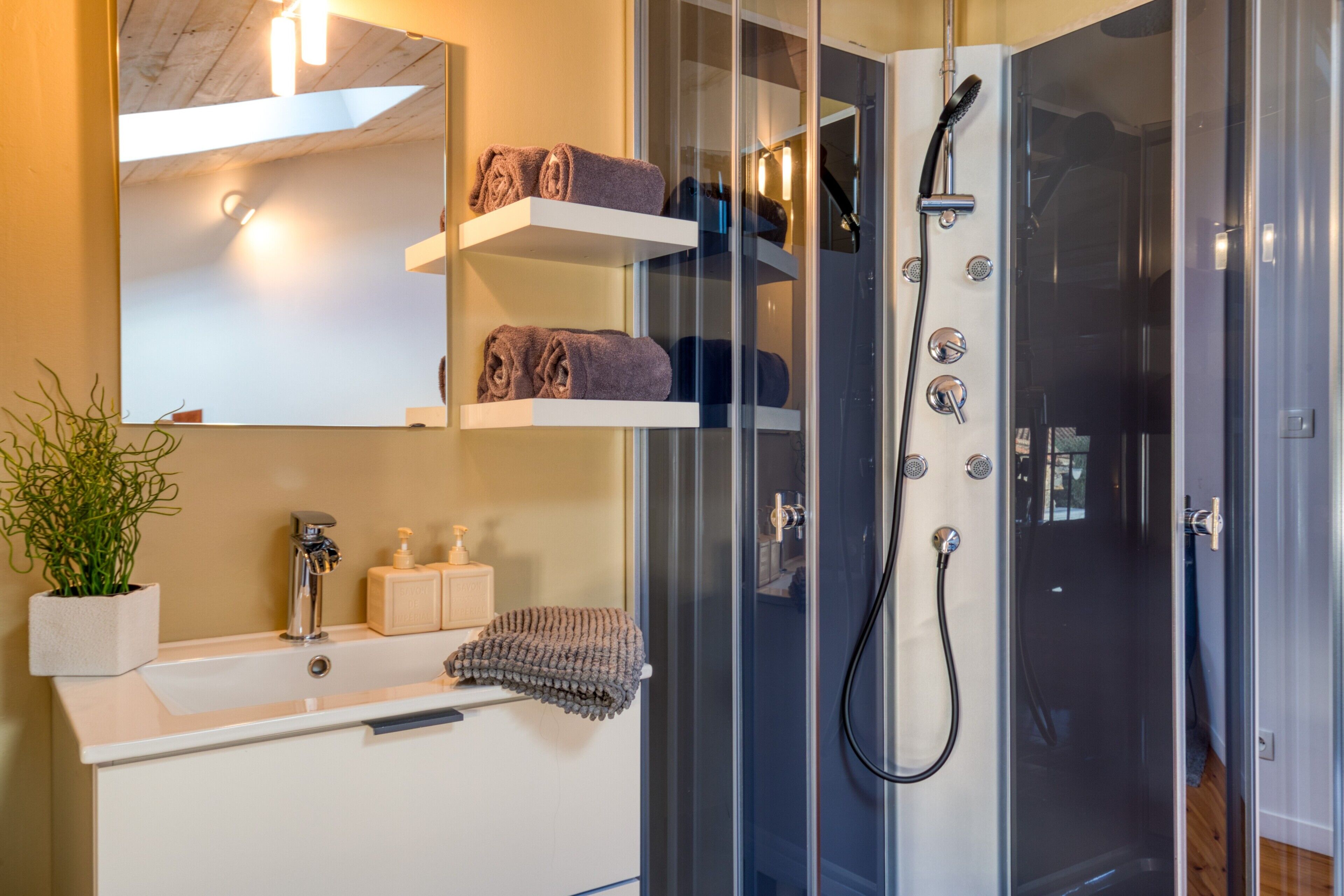 A modern bathroom with a glass-enclosed shower, a white sink, and shelves with towels.