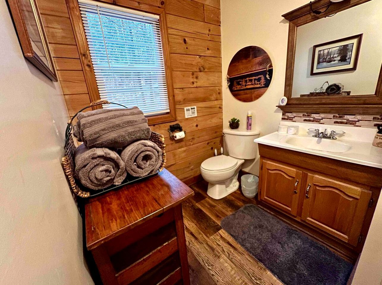 Une salle de bain avec des murs en bois, des toilettes, un lavabo avec un miroir et un porte-serviettes avec des serviettes.