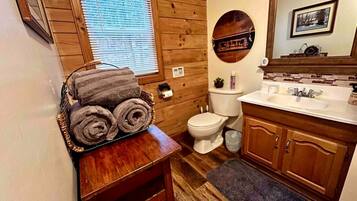 Une salle de bain avec des murs en bois, des toilettes, un lavabo avec un miroir et un porte-serviettes avec des serviettes.