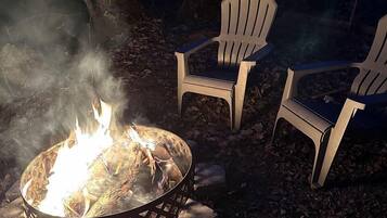 A campfire with chairs around it in a wooded area.