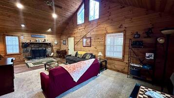 A cozy cabin interior with a fireplace, a sofa, a dining table, and a bookshelf.