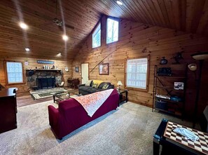 A cozy cabin interior with a fireplace, a sofa, a dining table, and a bookshelf. - Cozy Forest Cabin Surrounded by Trees near Stone Mountain State Park, North Carolina (Wilkes County)