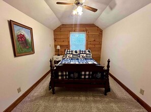 A bedroom with a wooden ceiling fan, a bed with a checkered bedspread, a nightstand, a window with blinds, and a framed picture on the wall. - Cozy Forest Cabin Surrounded by Trees near Stone Mountain State Park, North Carolina (Wilkes County)