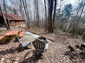A rustic cabin with a wooden deck, a fire pit, and two Adirondack chairs. - Cozy Forest Cabin Surrounded by Trees near Stone Mountain State Park, North Carolina (Wilkes County)