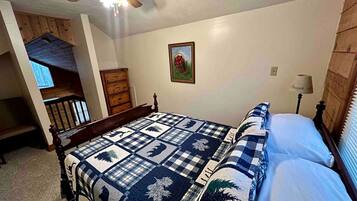 A bedroom with a bed, a ceiling fan, a wooden bench, a door, and a wall-mounted lamp.
