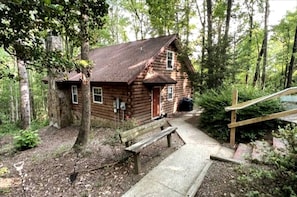 A rustic log cabin with a wooden deck, a bench, and a wooden staircase leading to the entrance. - Cozy Forest Cabin Surrounded by Trees near Stone Mountain State Park, North Carolina (Wilkes County)