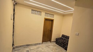 A hallway with a patterned floor, a wooden door, and a patterned sofa. - Rudra PGH - just near Temple & Ghats (Varanasi)