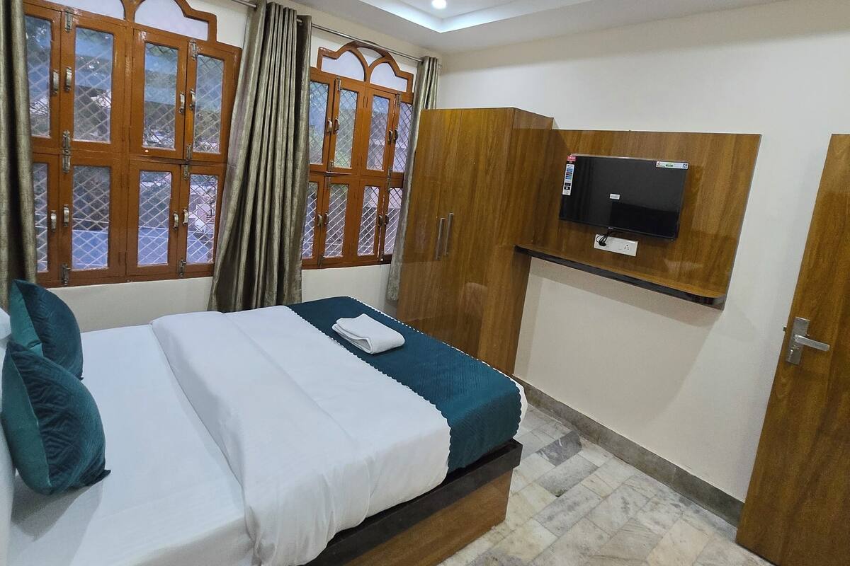 A bedroom with a bed, a ceiling fan, a TV mounted on the wall, and a window with curtains.