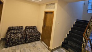 A living room with a patterned sofa set, a wooden door, and a staircase with a railing. - Rudra PGH - just near Temple & Ghats (Varanasi)