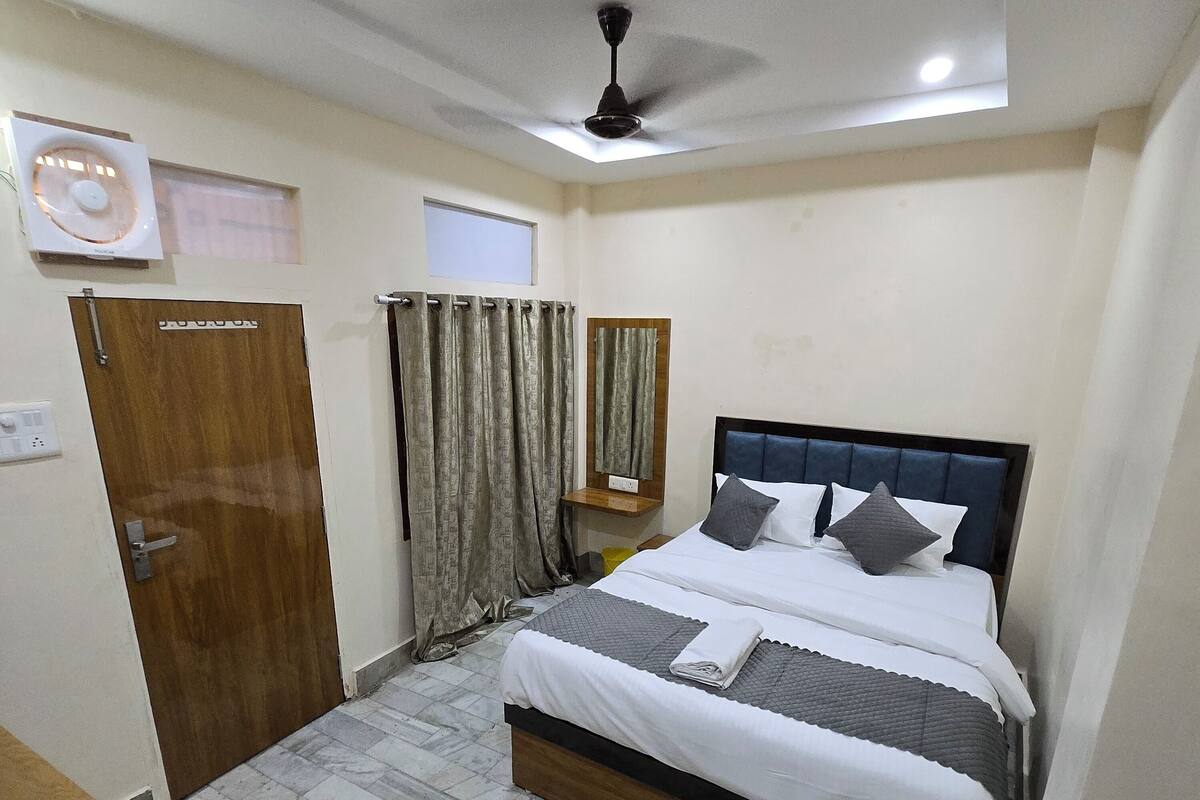 A bedroom with a bed, a ceiling fan, a wooden door, a mirror, and a small window.