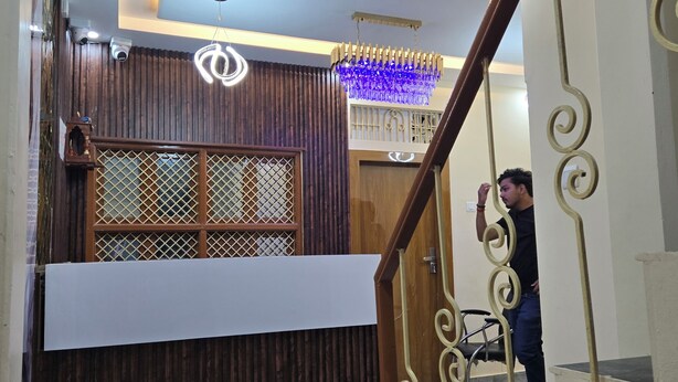 A reception area with a wooden reception desk, a chandelier, and a staircase with ornate railings. - Rudra PGH - just near Temple & Ghats (Varanasi)